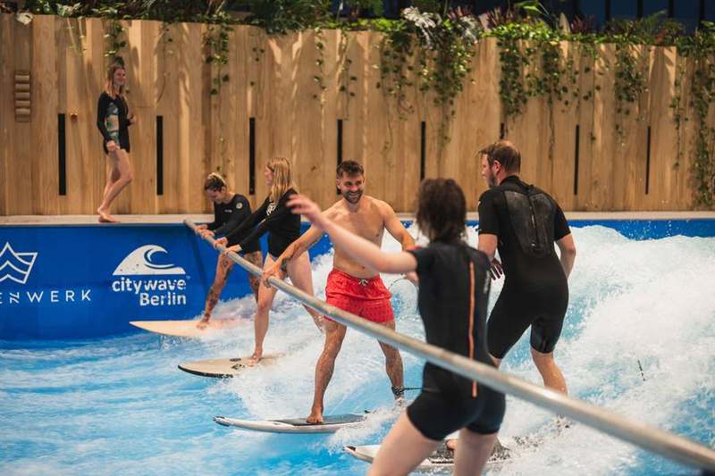Team beim Indoor-Surfen, lachend, Coach im Wasser